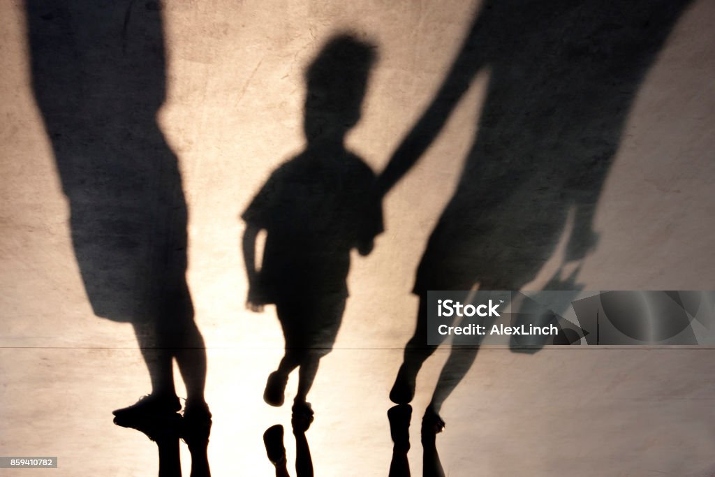 Blurry shadow of two person and a kid Blurry shadows of mother walking with son hand in hand and a man standing next to them Child Stock Photo