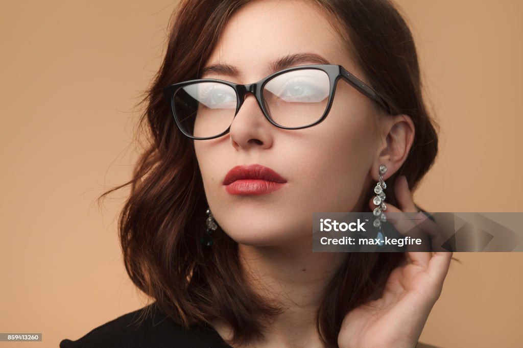 Beautiful woman in black rimmed spectacles Beautiful brunette woman wearing black rimmed spectacles touching drop earrings looking away. Eyeglasses Stock Photo
