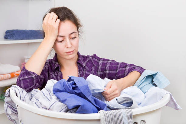 服でいっぱいのバスケットを持つ欲求不満の若い女性 - iron laundry cleaning ironing board ストックフォトと画像