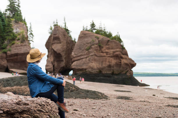 Seniors, woman looking at rocks, Hopewell, Bay of Fundy, New-Brunswick, Canada. <<Woman sitting on a rock an looking at geology formations created by erosion.>> double denim stock pictures, royalty-free photos & images