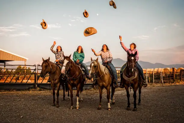 Group of young women throwing up their cowboy hats into the air while sitting on their horse.