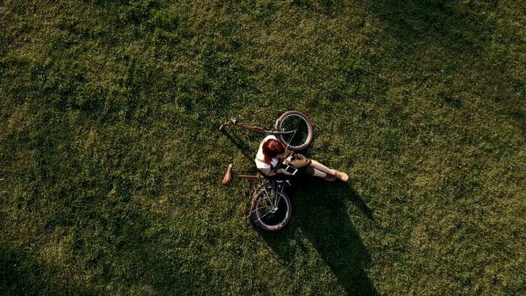 Drone view woman cyclist lying on green grass and using mobile phone