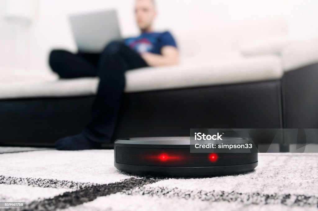 Robotic vacuum cleaner on carpet. Robotic vacuum cleaner working on carpet. Abstract science fiction red eyes sensor concept Vacuum Cleaner Stock Photo