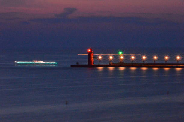 A long exposure of a light house on a pier near the beach of South Haven MI with a ship coming in.
