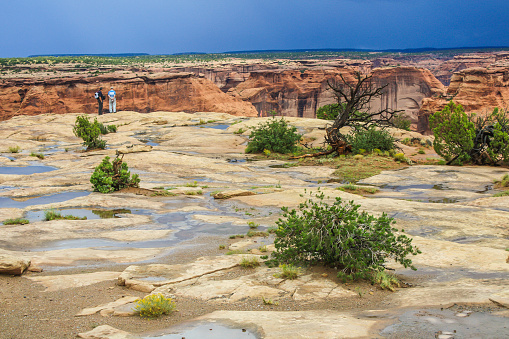 Two tourists in the distance look down into the vast chasm of Canyon de Chelly National Monument in Arizona in the summer of 2008