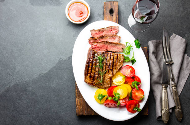 istock Sliced medium rare grilled beef steak served on white plate with tomato salad and potatoes balls. Barbecue, bbq meat beef tenderloin. Top view, slate background, copy space 859485846