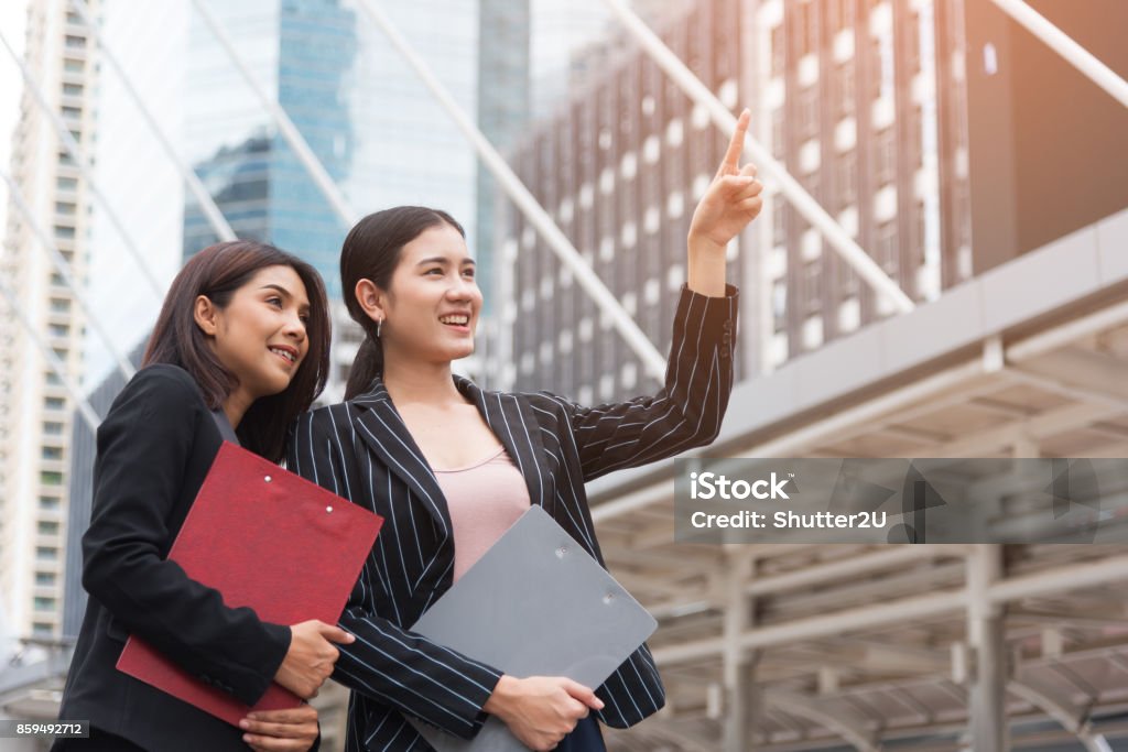 Two young beautiful business women pointing and smiling with outdoor background. Business and beauty concept. Meeting and Greeting concept Adult Stock Photo