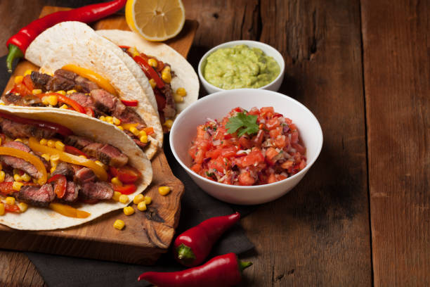 istock Three Mexican tacos with marbled beef, black Angus and vegetables on old rustic table. Mexican dish with sauces guacamole and salsa in bowls 859504262