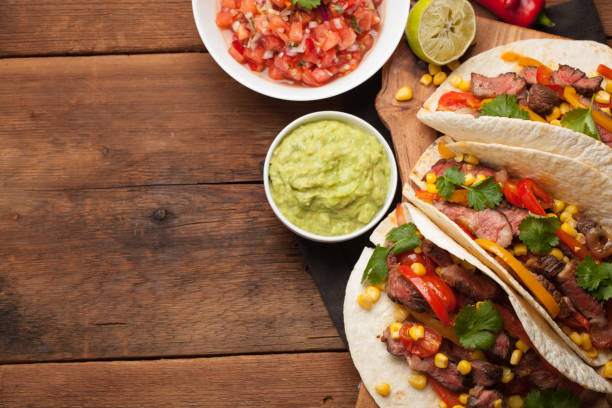 istock Three Mexican tacos with marbled beef, black Angus and vegetables on old rustic table. Mexican dish with sauces guacamole and salsa in bowls. Top view with copy space 859504290