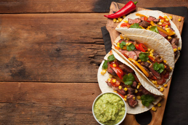 istock Three Mexican tacos with marbled beef, black Angus and vegetables on old rustic table. Mexican dish with sauces guacamole and salsa in bowls. Top view with copy space 859504318