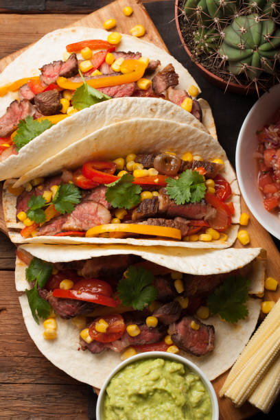 istock Three Mexican tacos with marbled beef, black Angus and vegetables on old rustic table. Mexican dish with sauces guacamole and salsa in bowls. top view 859504322