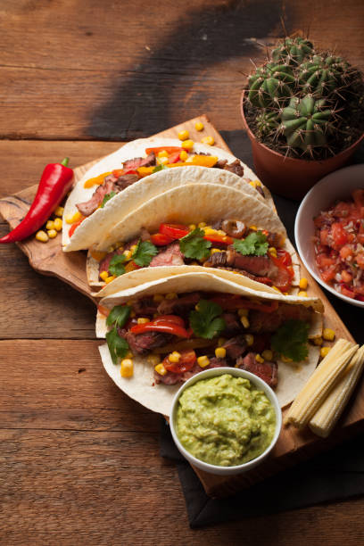 istock Three Mexican tacos with marbled beef, black Angus and vegetables on old rustic table. Mexican dish with sauces guacamole and salsa in bowls. top view 859504338