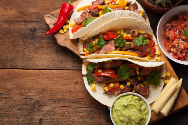 istock Three Mexican tacos with marbled beef, black Angus and vegetables on old rustic table. Mexican dish with sauces guacamole and salsa in bowls. Top view with copy space 859504346