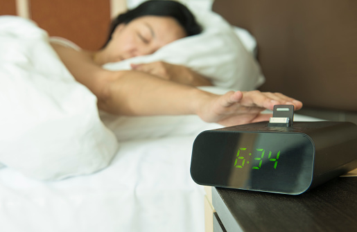 Young woman reach out one's hand Press the button to turn off the digital alarm clock in morning.