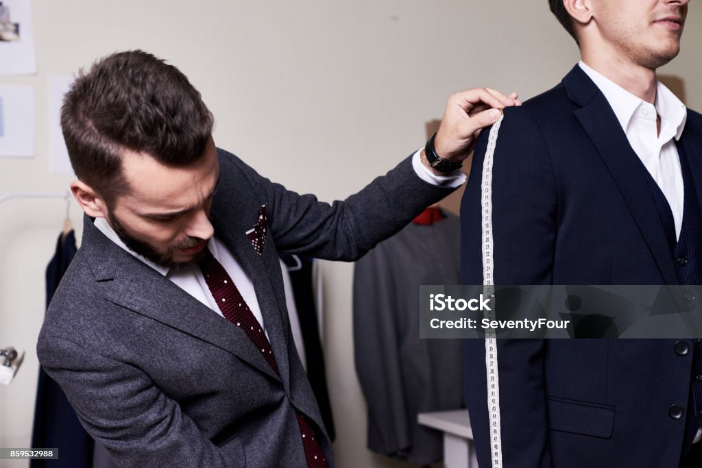 Model Fitting in Traditional Atelier Portrait of modern tailor measuring arm length of bespoke suit during model fitting in traditional atelier studio Tailor Stock Photo