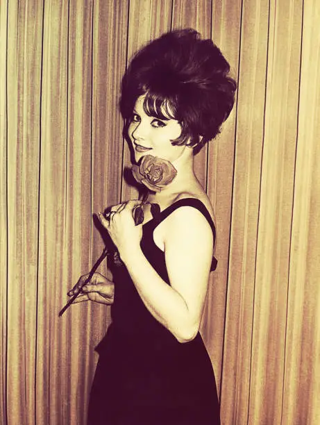 Vintage black and white photo from the sixties of a young woman holding a rose and looking at camera.
