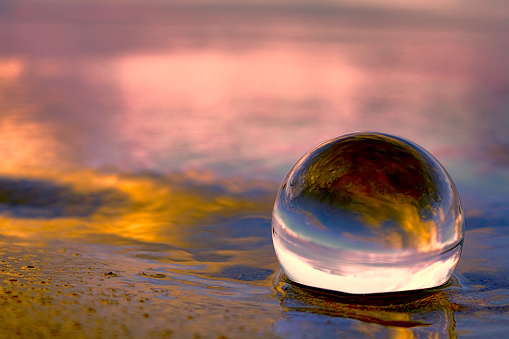 Summer sunset displayed through a transparant glass ball on the beach sand