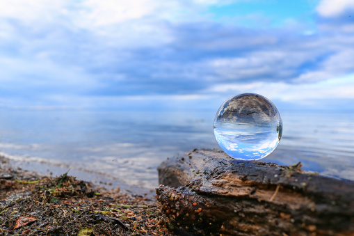 Transparent glass ball on a log reflecting calm blue water of Cold Lake, Alberta