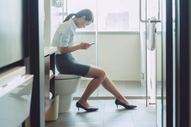 woman sitting on flush toilet typing smartphone stock photo