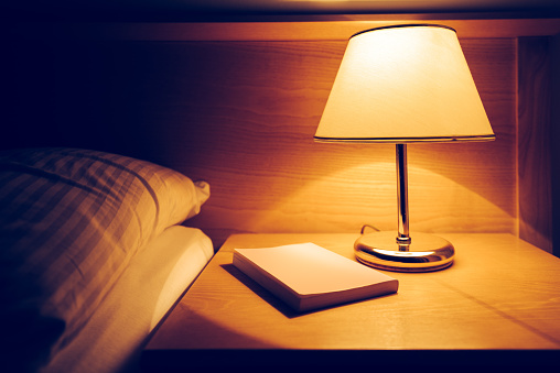 Book and lamp on night table in hotel room next to the empty bed and pillow