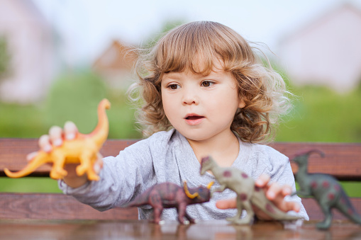 Little girl having fun playing with plastic dinosaurs outdoors.
