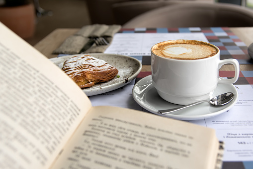 Still life details, cup of Cappuccino and cake with book on table in coffee shop cafe, shallow DOF.