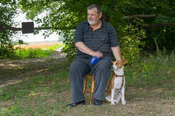 istock Man sitting on a stool next to his four-legged friend (basenji dog) in summer park 859607624