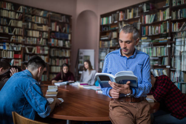 istock Mid adult teacher reading a book in the library. 859612260