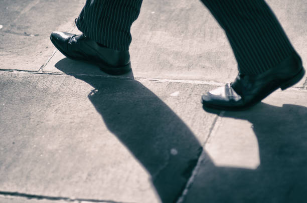 Close-up of well-dressed businessman in pinstriped suit and business shoes walking with shadow on the city sidewalk