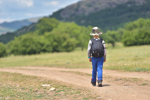 Cute child boy with backpack walking on a little path in mountains. Hiking kid