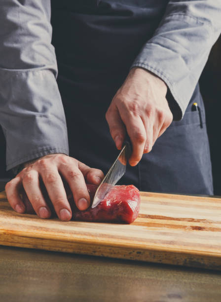 istock Chef cutting filet mignon on wooden board at restaurant kitchen 859631546