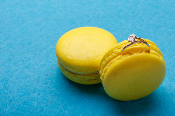 A diamond ring in yellow macaroon over blue background. the offer to marry. place for text A diamond ring in yellow macaroon on blue background. the offer to marry. place for text wedding cake close up macro stock pictures, royalty-free photos & images