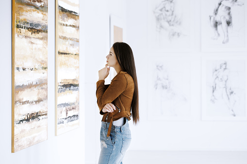 Young woman observing painting while visiting art gallery with famous artist collection