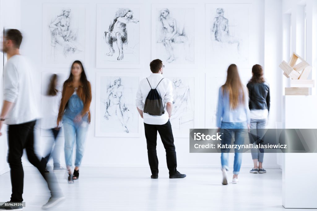 Man with rucksack in gallery Young man with rucksack on back visiting art gallery with drawings and sculpture Art Museum Stock Photo