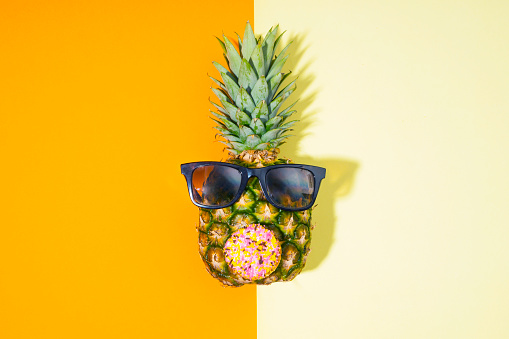 Pineapple with sunglasses on yellow and orange Colored paper background.Pineapple and  sunglasses on papers in a geometric flat composition