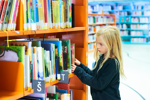 Child girl in public library with book