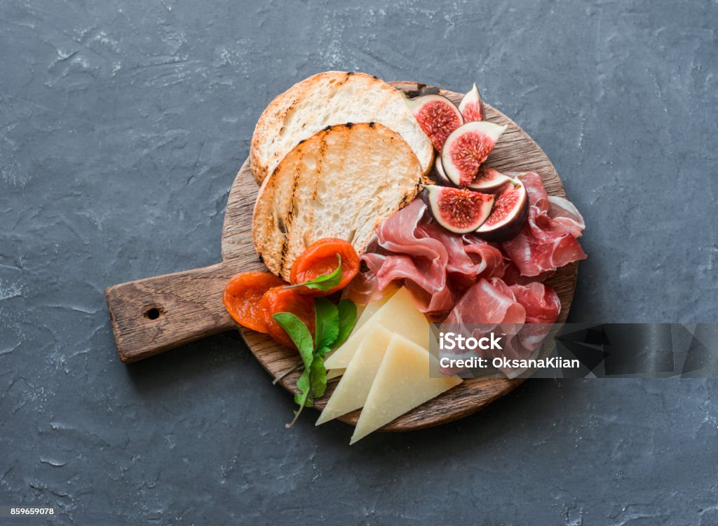 Delicious appetizers for wine or a snack - prosciutto, figs, bread, cheese on a rustic wooden cutting board. On a gray background, top view Cheese Stock Photo