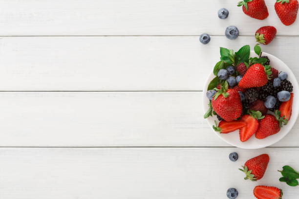 istock Mixed berries in glass bowls on white wooden table top view 859662448