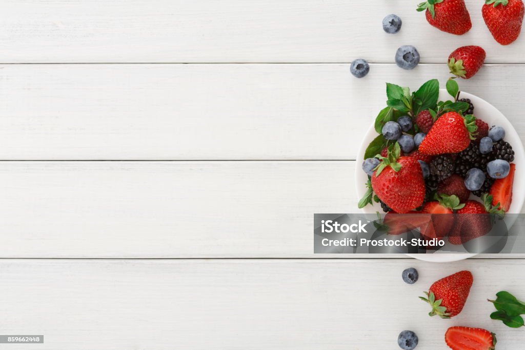 Mixed berries in glass bowls on white wooden table top view Assorted garden and wild berries background. Mix of fresh organic strawberries, raspberries, blueberries and blackberries in glass bowl on white wooden table, top view, copy space Berry Stock Photo