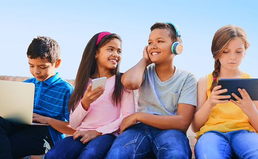 Shot of a diverse group of children having fun with technology outside