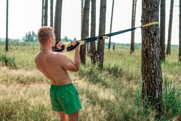 istock Male athlete excellent training training loops, fresh air nature in summer forest, feel your strength, motivation. Exercise of the biceps muscles. A sunny day. Stamina man. Against background of trees. 859664982