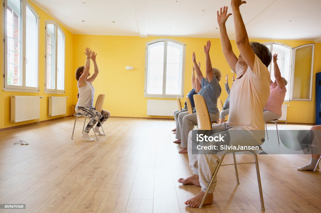 Teacher and active senior women yoga class on chairs Teacher and active senior women yoga class on chairs, arms raised, Senior Adult Stock Photo