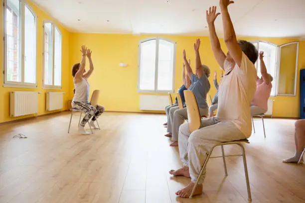 Photo of Teacher and active senior women yoga class on chairs