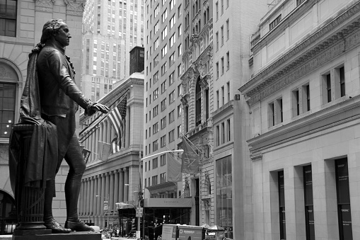 New York City, USA - September 09, 2017: Washington holds American flag in front of Federal Hall on Wall Street in New York City. In the background buildings of Wall Street - among others Tiffany & Co store.