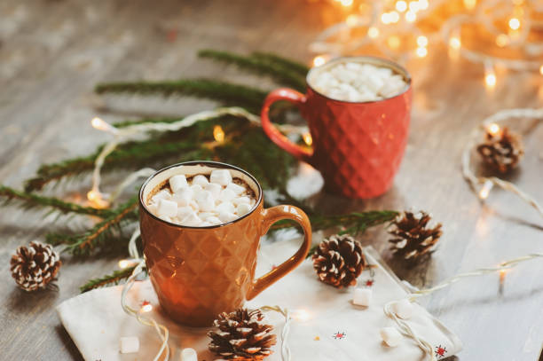 istock two mugs of hot cocoa with marshmallows on rustic wooden table with christmas lights. Cozy winter festive home concept 859675974