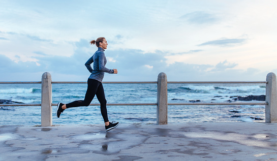 Side view of fitness woman running on a road by the sea. Sportswoman training on seaside promenade.