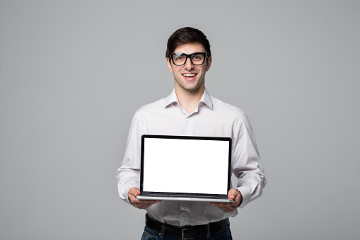 Smiling businessman pointing finger on blank laptop screen over gray background. Looking at camera
