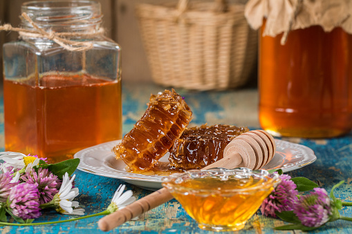 Two honey pots with honeycomb and bee pollen on a wooden table  with flowers. Horizontal composition