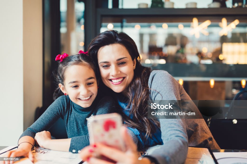 Mother and daughter in restaurant taking photos Young mother and cute daughter taking selfies in cafe Christmas Stock Photo