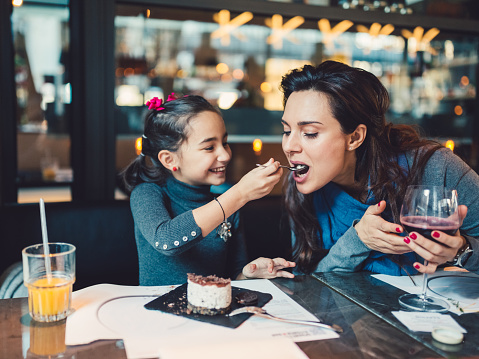 Young mother and cute daughter eating lunch in restaurant